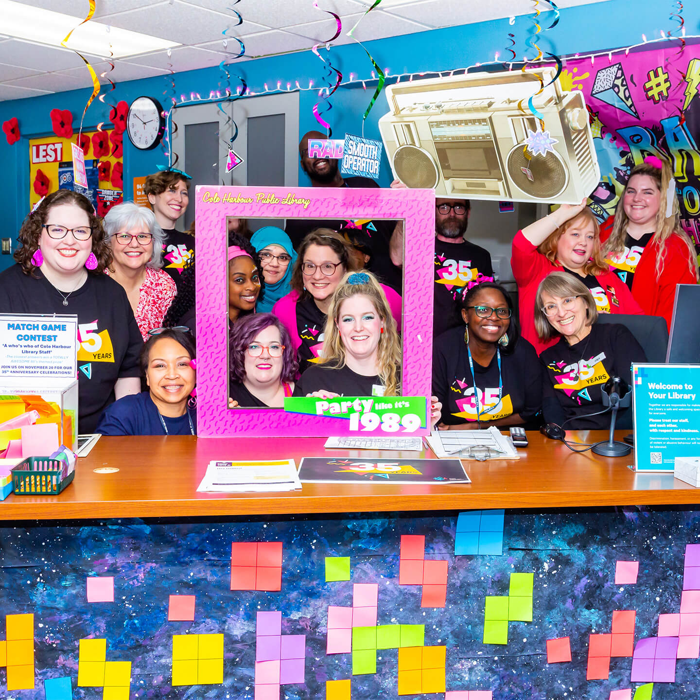Library staff smiling for a group photo at the 80s themed anniversary.